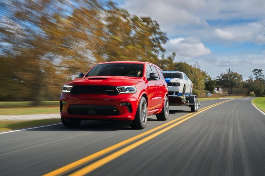 Front 3/4 view of the 2021 Dodge Durango SUV towing a Dodge Challenger on the road.