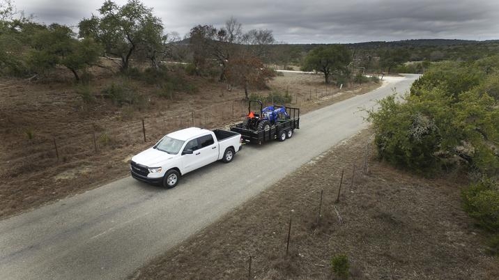 RAM 1500 Tradesman 2020, design blanc, remorquant un tracteur, conduisant sur une route de terre