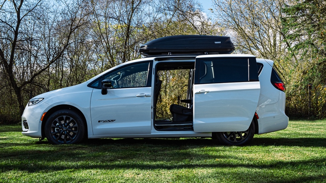 Vue latérale du Chrysler Pacifica 2025 blanc avec porte coulissante ouverte et coffre de toit, idéal pour les longs trajets familiaux.