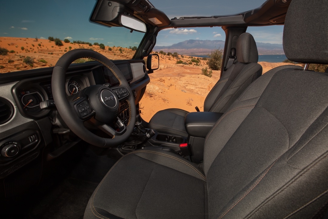 Intérieur du Jeep Wrangler 2025 avec toit ouvert, volant Jeep et sièges en tissu foncé, vue sur désert et montagnes au loin.
