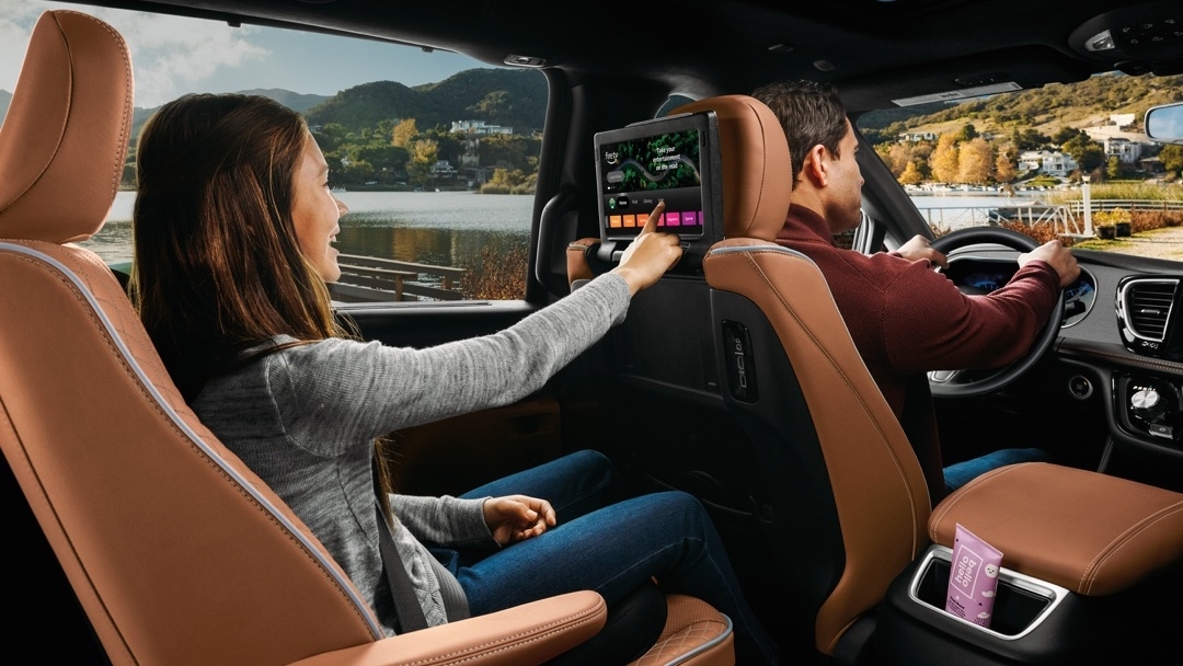 Passagère arrière utilisant l’écran tactile du système de divertissement du Chrysler Pacifica 2025, démontrant le confort familial en voyage.