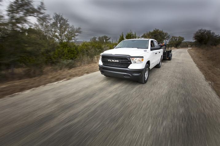 RAM 1500 Tradesman 2020, design blanc, remorquant un tracteur, conduisant sur une route de terre