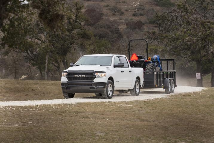 RAM 1500 Tradesman 2020, design blanc, remorquant un tracteur, conduisant sur une route de terre