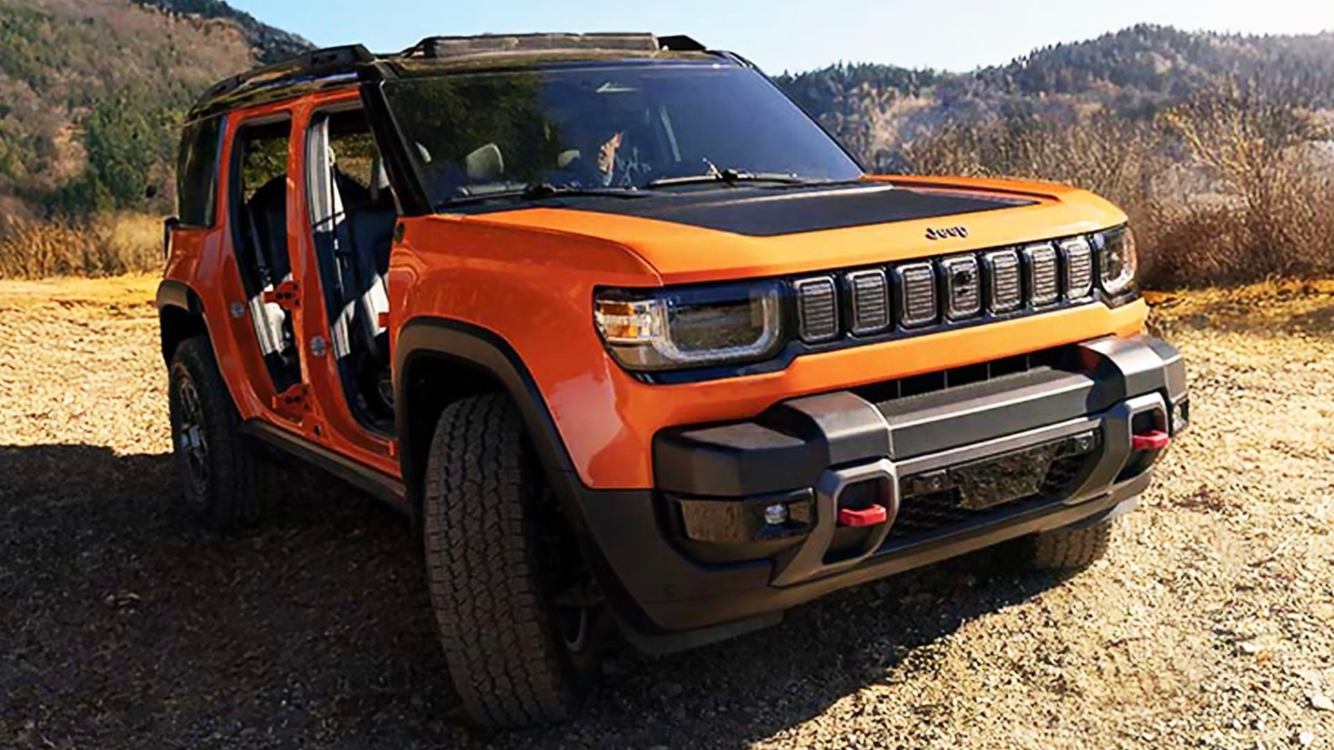 Jeep Recon 2026 orange sans portières garé sur un chemin de gravier, en pleine nature. Vue de face.