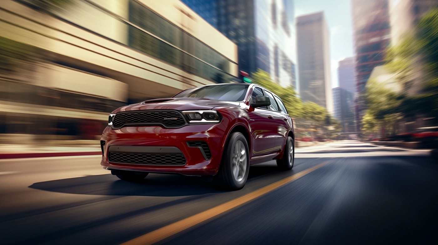 Red Dodge Durango GT 2025 driving in the city on a clear road.