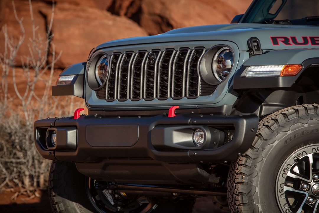 Gros plan sur la calandre et le pare-chocs du Jeep Wrangler Rubicon 2025 gris, mettant en avant le logo et les crochets de remorquage rouges.