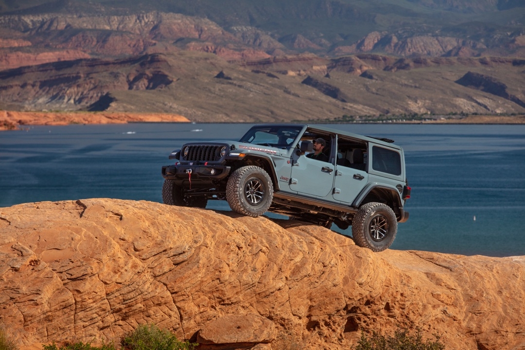 Jeep Wrangler Rubicon 2025 gris clair en montée rocheuse près d’un lac, illustrant sa puissance et ses aptitudes en escalade hors route.