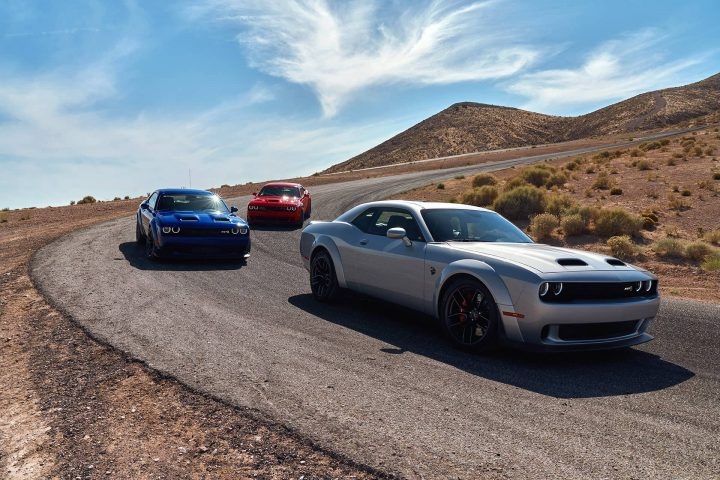 trois Dodge Challenger SRT 2020 se suivant sur un chemin dans un désert avec différentes éditions de couleur; rouge (en arrière), bleu (milieu) et le gris (à l'avant)