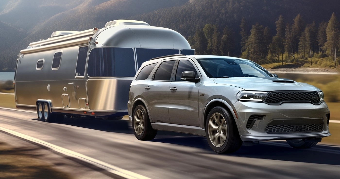 Gray Dodge Durango 2025 towing a trailer on a country road.