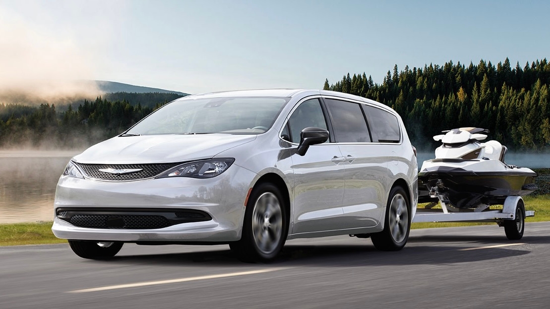 Chrysler Grand Caravan 2025 blanc tractant une motomarine sur route, démontrant sa capacité de remorquage familiale.