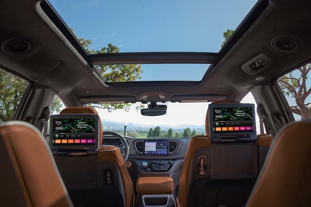 Habitacle de la Chrysler Pacifica 2026 avec sièges en cuir brun, écrans multimédias arrière et toit panoramique vitré offrant une vue dégagée.