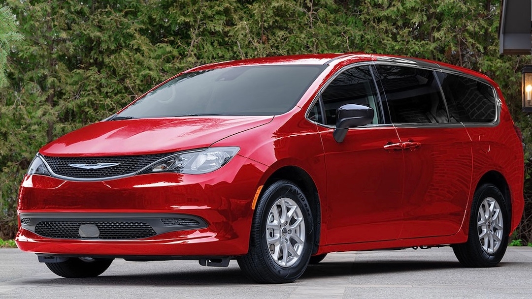 Chrysler Grand Caravan 2025 rouge de trois quarts avant, garé devant une maison, mettant en avant son style pratique et accessible.