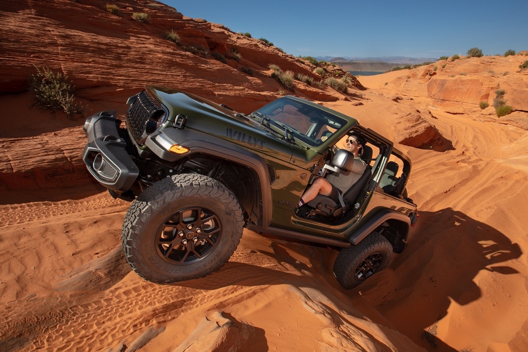 Jeep Wrangler Willys 2024 vert olive en conduite hors route sur sable rouge, démontrant ses capacités tout-terrain robustes.