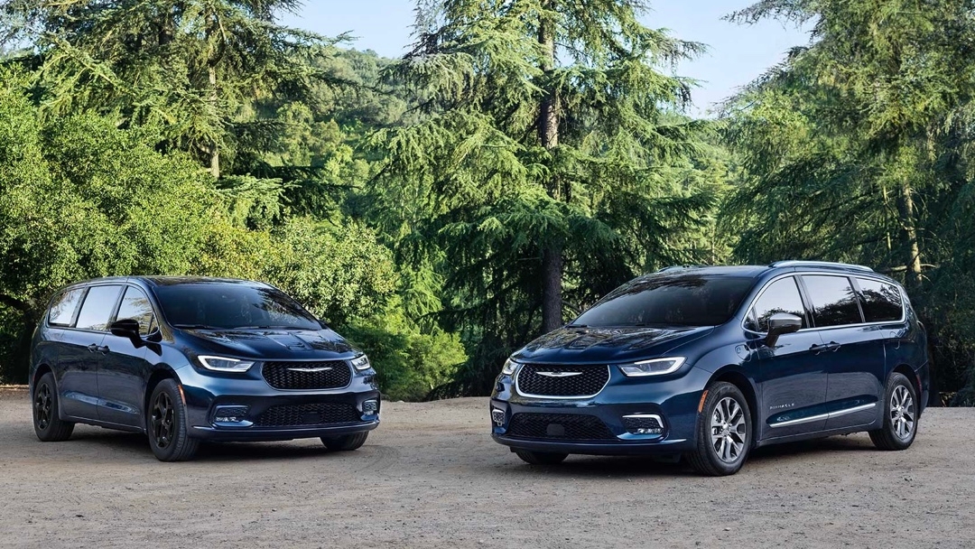Vue avant de deux Chrysler Pacifica 2025 bleus stationnés en forêt, illustrant les versions hybride rechargeable et essence.
