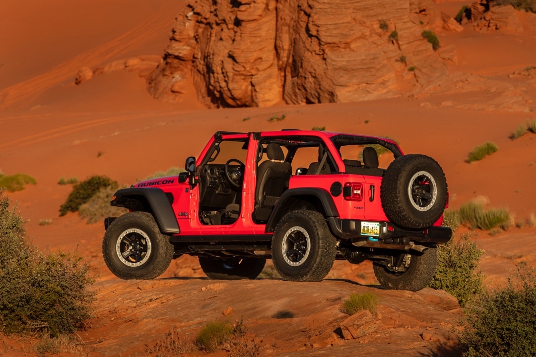 Jeep Wrangler 4xe 2025 Rubicon rouge photographié de l’arrière, portières retirées, sur terrain sablonneux dans le désert.
