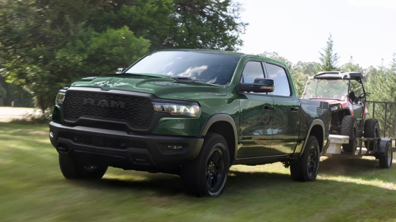 Ram 1500 Rebel 2026 vert remorquant un véhicule côte-à-côte sur une remorque, roulant sur chemin herbeux.