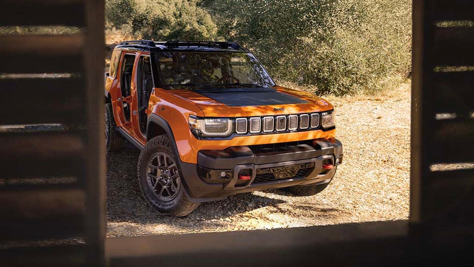 Jeep Recon VEB 2026 orange vu à travers une ouverture de cabane en bois. Stationné en forêt. Vue esthétique.