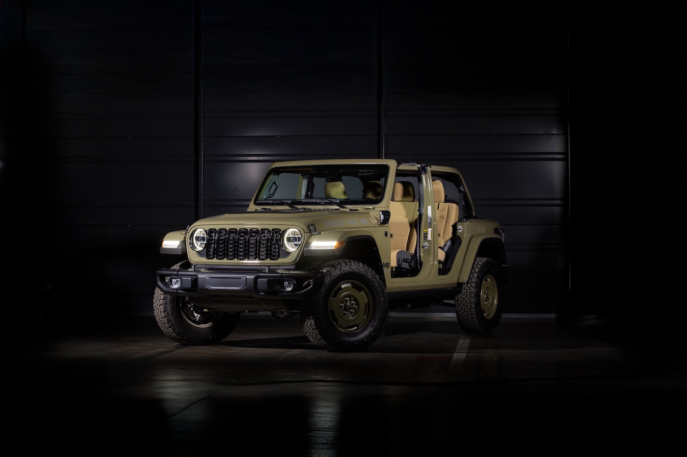 Jeep Wrangler 4xe 2025 Willys beige à l’intérieur d’un studio sombre, éclairage centré sur le véhicule.