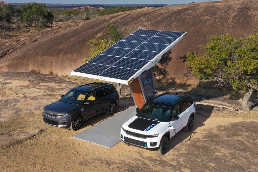 Two Jeep Grand Cherokee 4xe connected to a solar charging station in a rocky landscape.