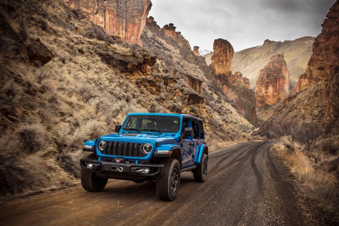 Jeep Wrangler 4xe 2025 Rubicon bleu roulant dans un canyon désertique avec parois rocheuses.