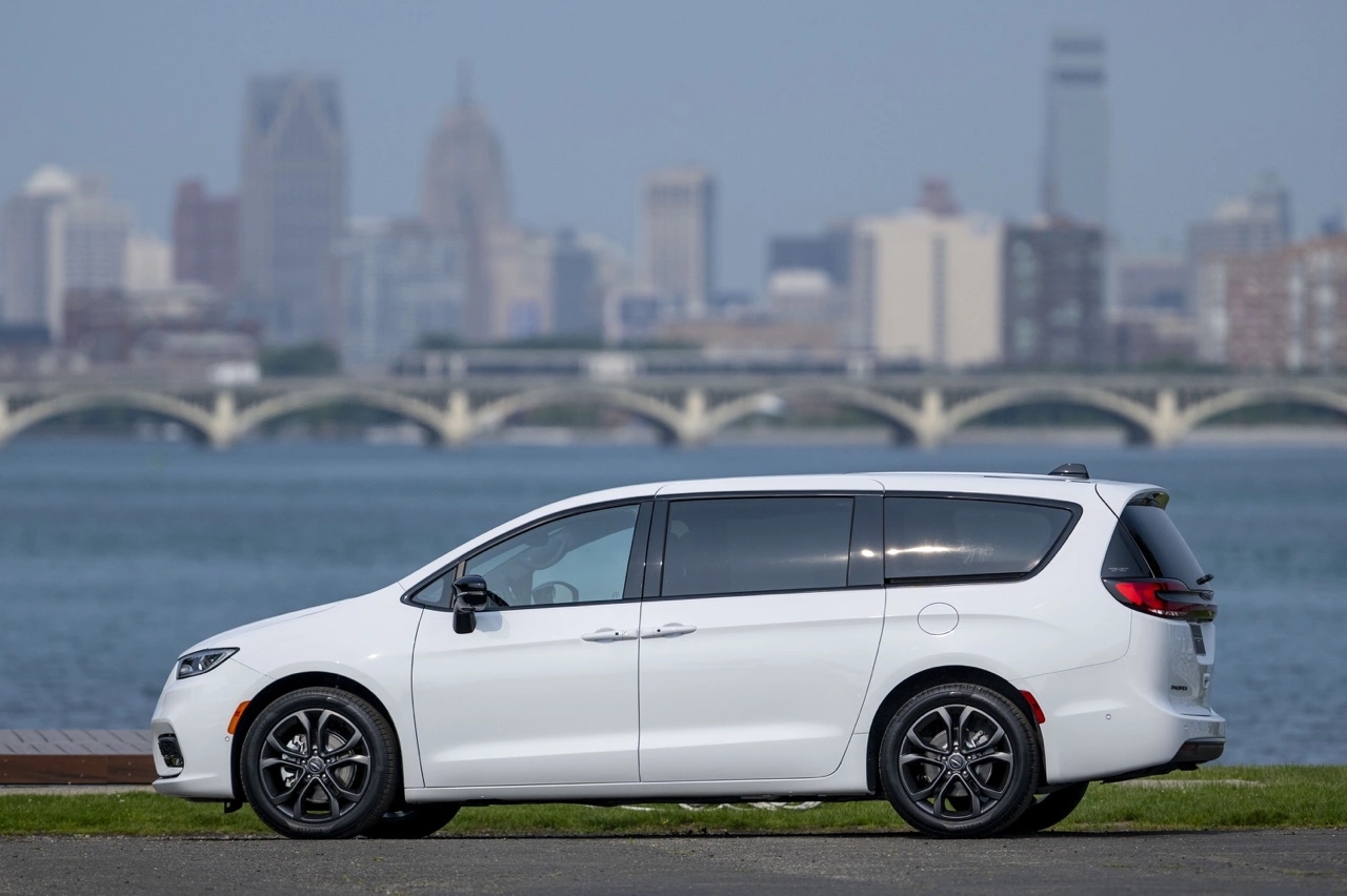 Chrysler Pacifica 2026 blanche vue de profil stationnée près d’un plan d’eau, avec pont et gratte-ciel en arrière-plan.