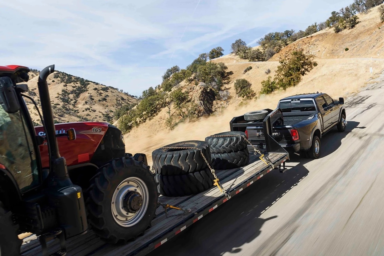 Vue arrière d’un Ram 3500 2026 tirant une remorque chargée d’équipement lourd sur route montagneuse, démontrant sa capacité de charge et de traction.