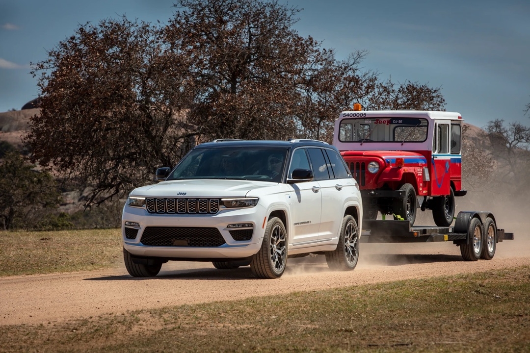 Jeep Grand Cherokee 4xe pulling a trailer with an old red and blue Jeep model.